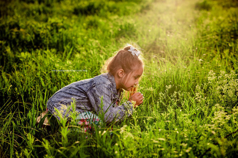 girl leaning over melling flowers in sunny green field