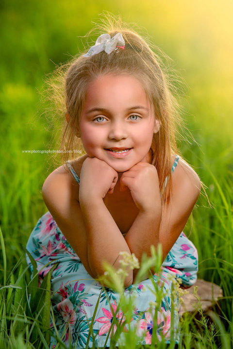 Young girl sitting in green field with hands on chin