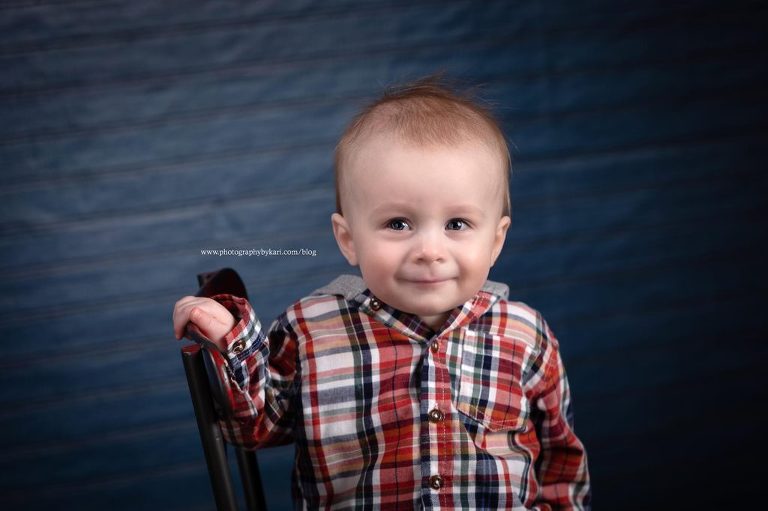 Infant boy sitting on red chair with smirk on his face