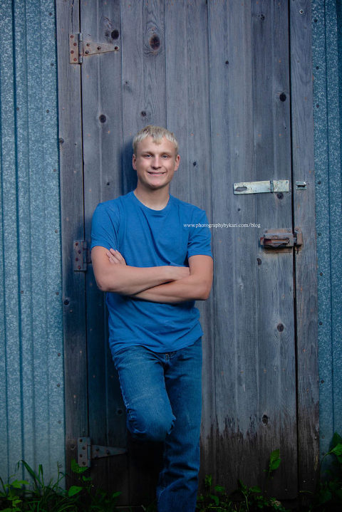 blonde senior farm boy leaning on tin shed