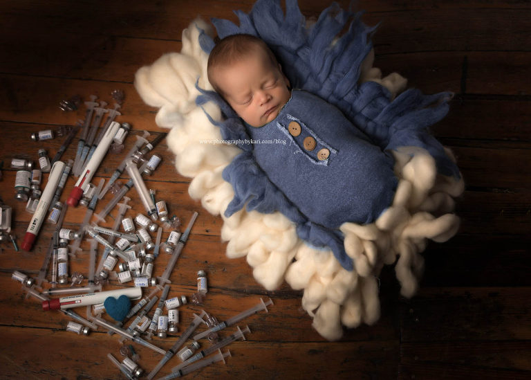 newborn boy in blue wrap with IVF needles and heart