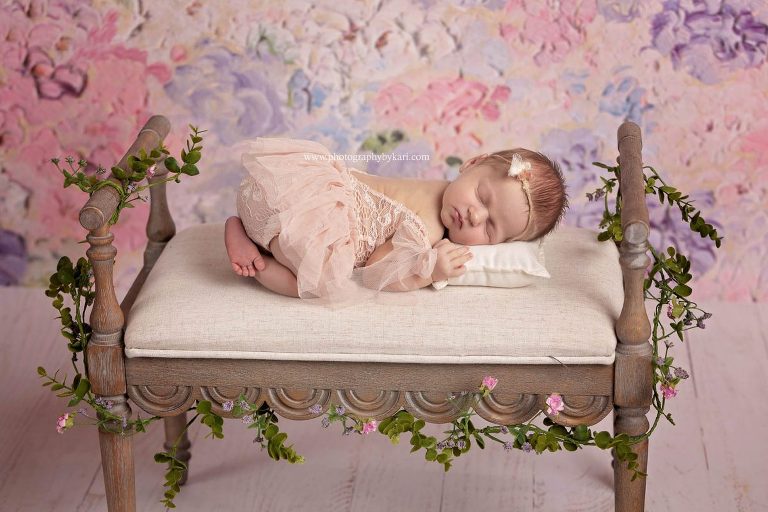 Newborn girl laying on bench with flowers photographe by Photography by Kari