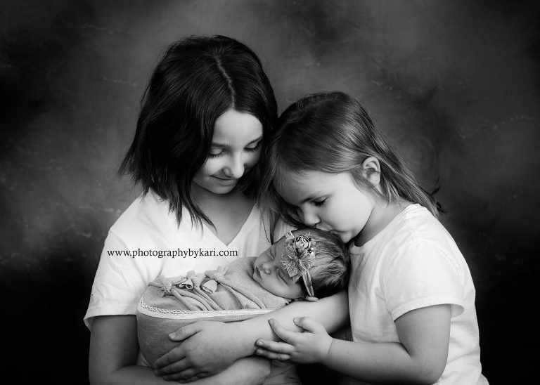 Newborn girl portrait with big sisters kissing