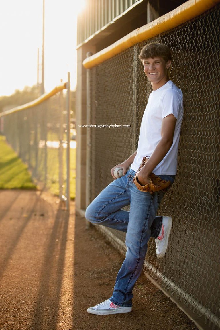 Senior guy portrait standing leaning on baseball dugout fence