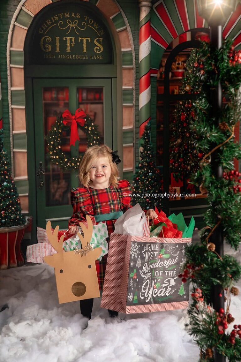 christmas mini photo of little girl holding holiday shopping bags taken in studio by photography by kari