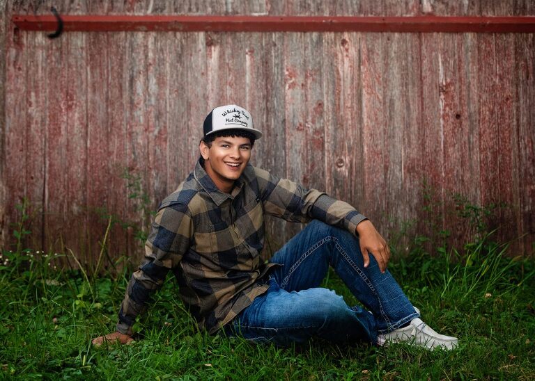 Guy Senior Portraits MN on red barn wood sitting in grass taken by Photography by Kari