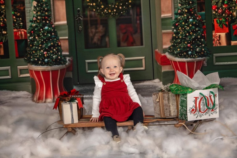 SE Minnesota Christmas Mini Portrait of baby girl sitting on sled with gifts taken in studio at Photography by Kari