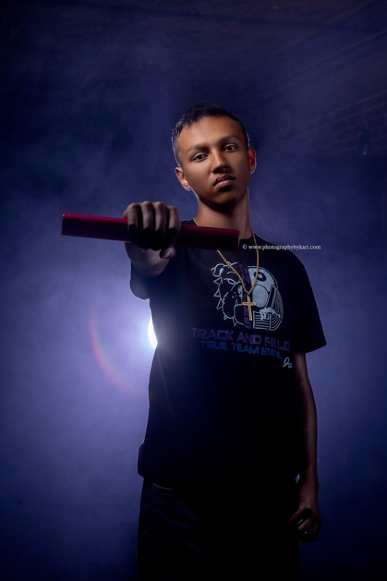 2025 senior boy posing with track medals and colored lighting