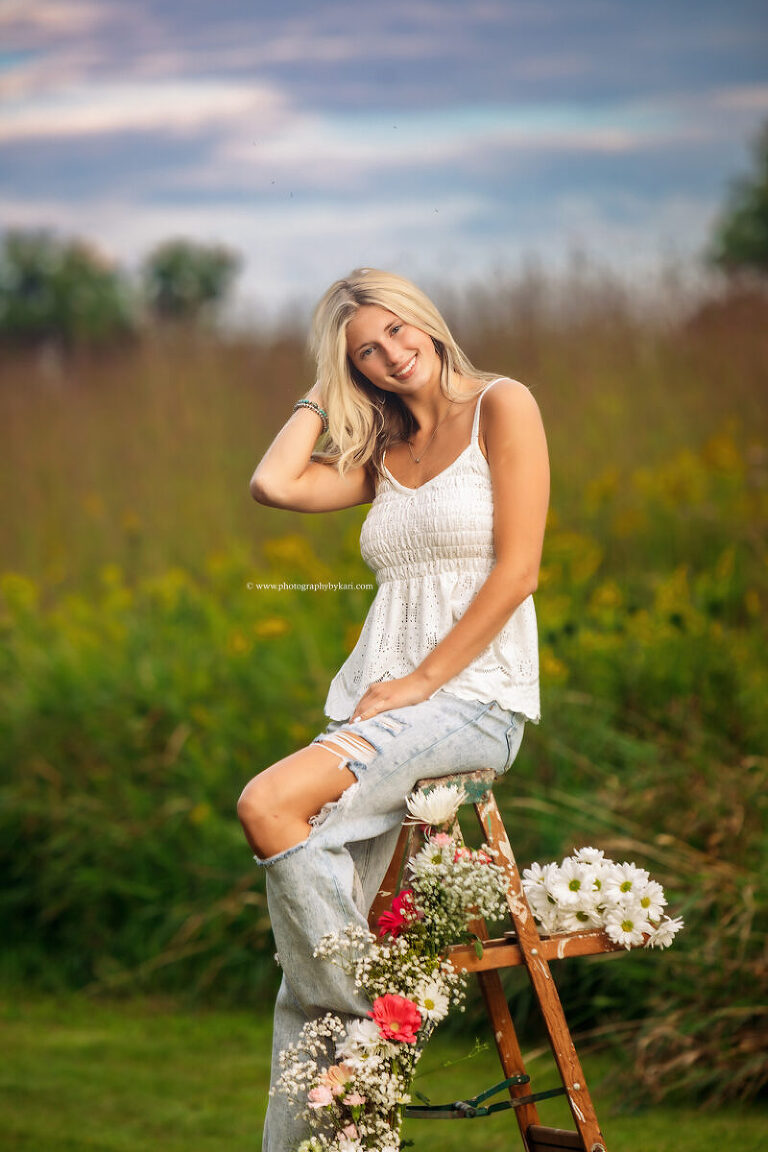 Cassie leaning on rustic ladder surrounded by wildflowers and tall grass