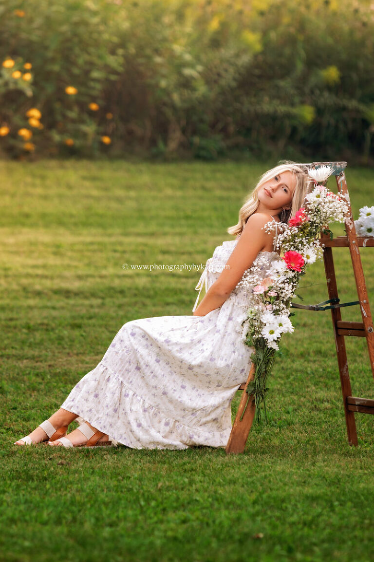 Cassie leaning on rustic ladder surrounded by wildflowers and tall grass in rural spring valley MN