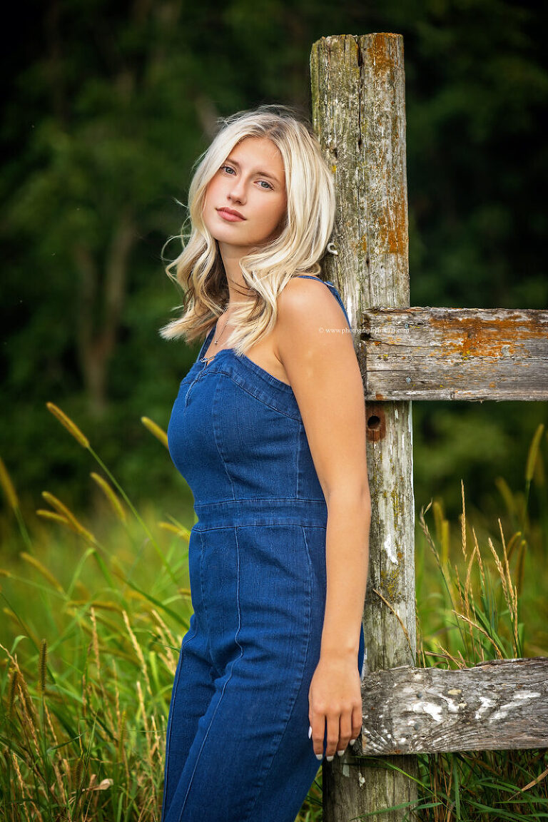 Cassie leaning on rustic post surrounded by wildflowers and tall grass