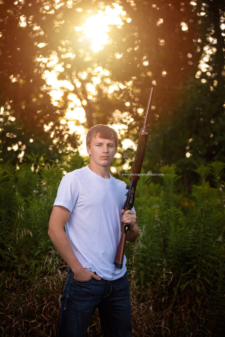 Seth posing with family hunting rifle for senior photo on rural property in southeast minnesota