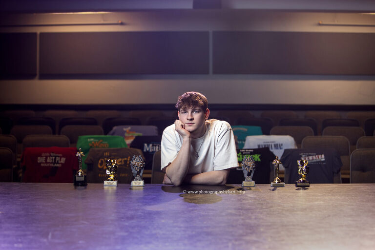 Senior boy with one act play trophies and spring musical shirts in theater auditorium