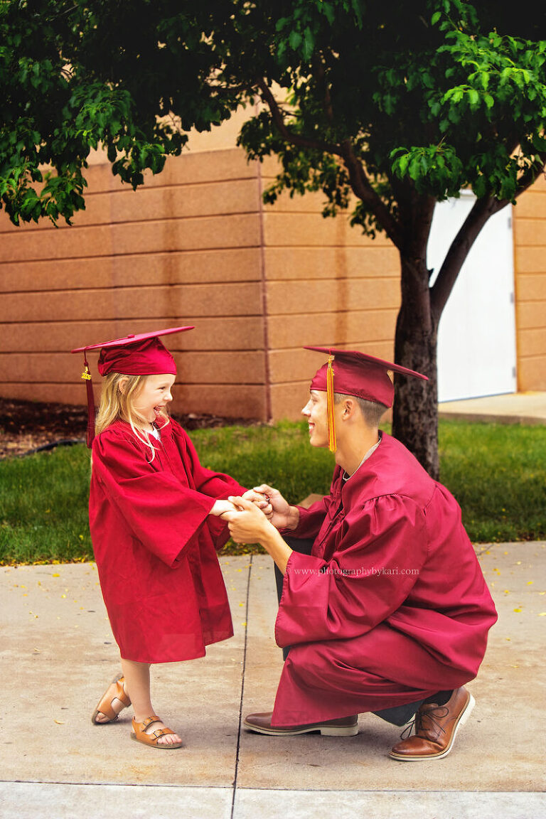 Senior graduate and younger sister wearing matching graduation caps and gowns